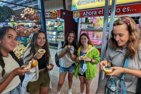 A group of girls hold a fruit and smile at the camera.